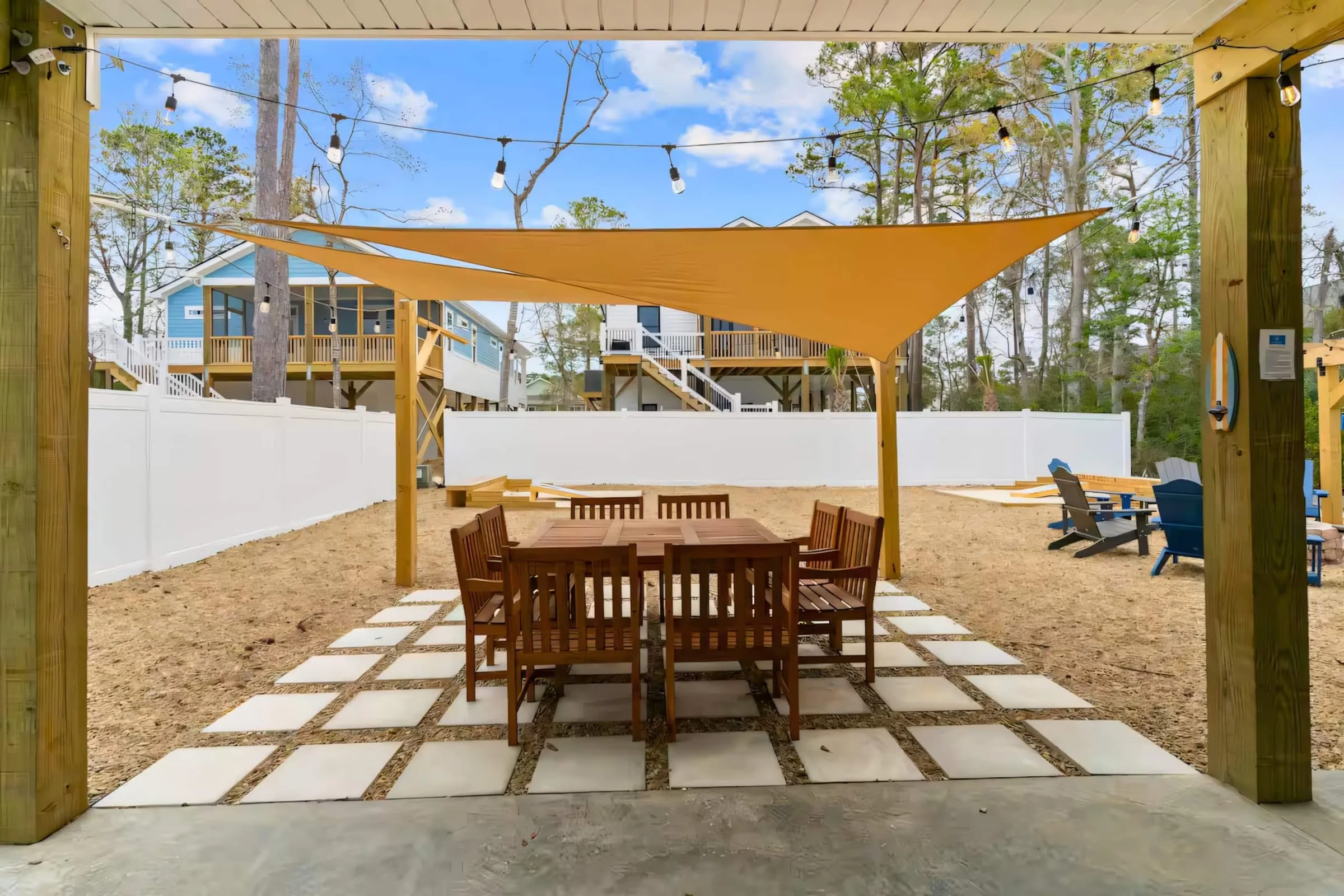 Backyard dining table under a wooden pergola with shade sails and string lights