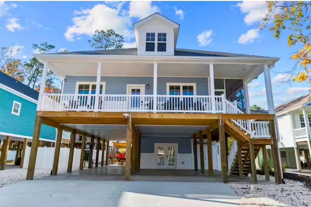 Front of the raised blue beach cottage with white trim, a wide porch, and palms out front