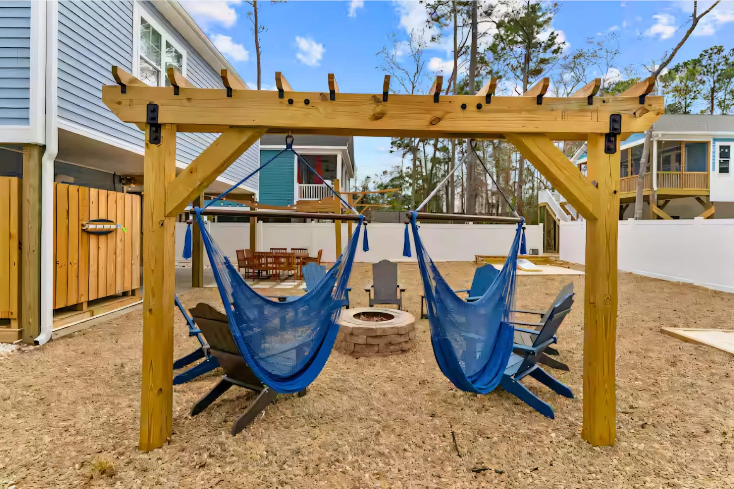 Two blue hammocks hanging from the pergola with the fire pit beyond
