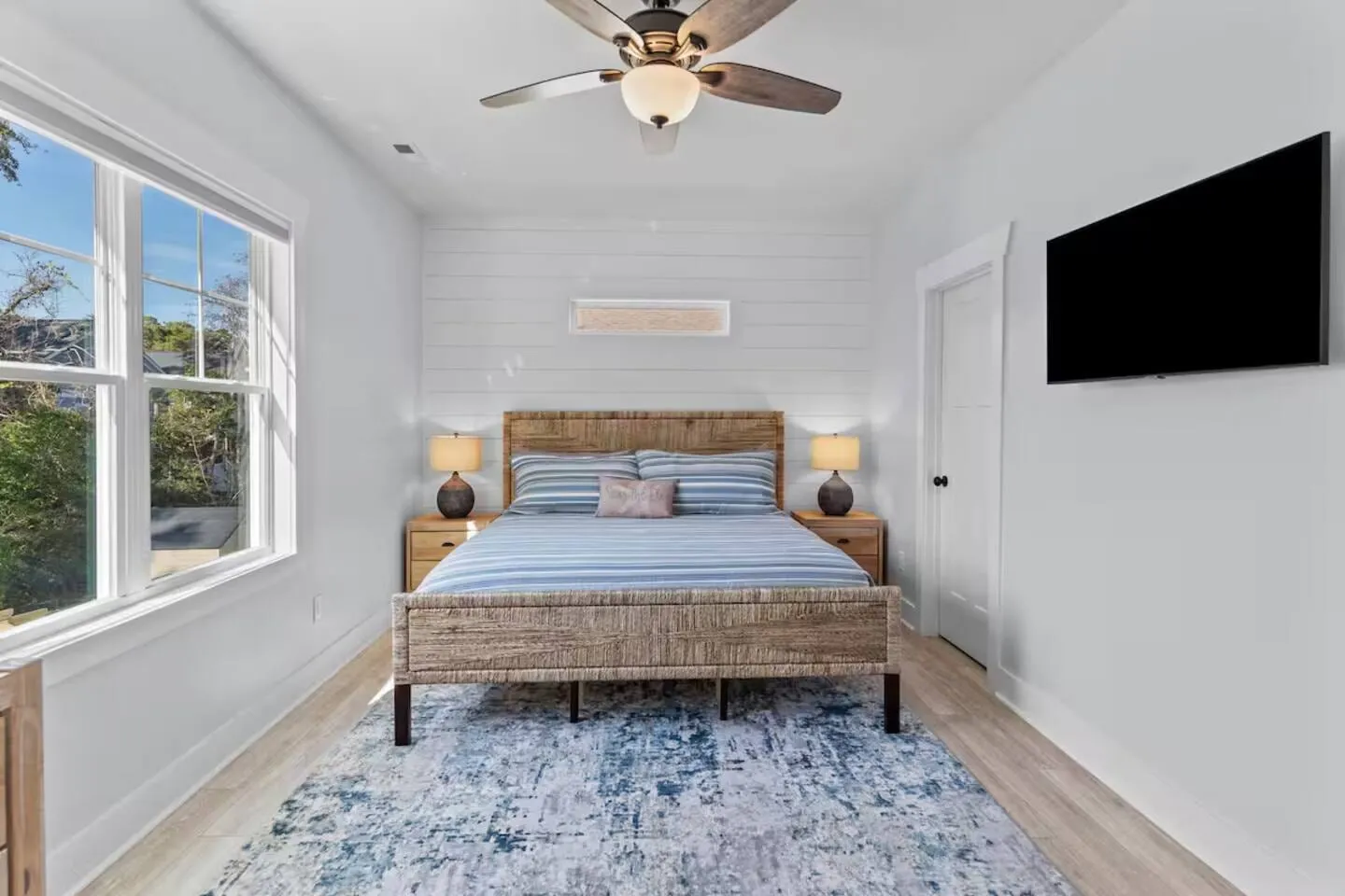 King master bedroom with a light wood bed, blue linens, shiplap wall, and ceiling fan